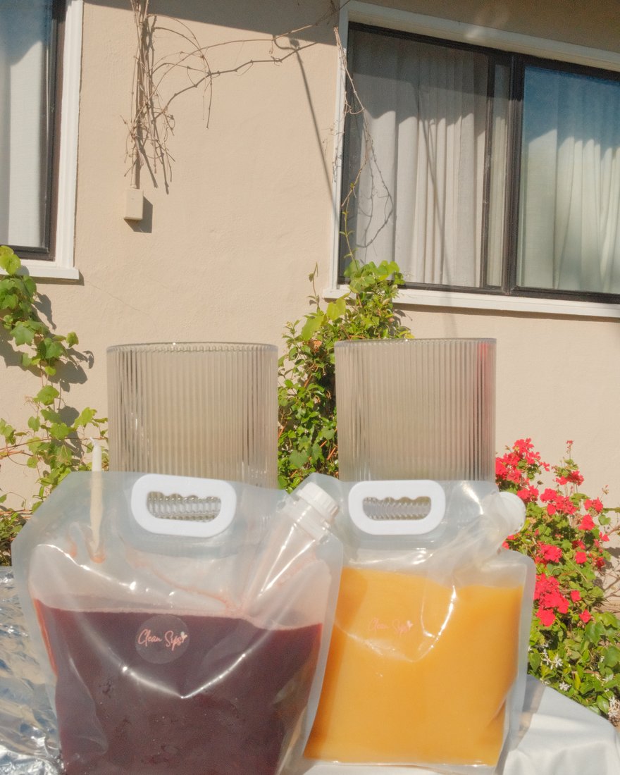 Two Clean Sips gallon pouches in pomegranate and mango, with drink dispensers ready behind them